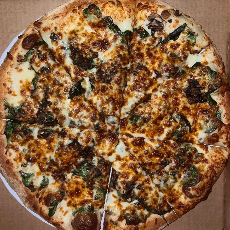 Raven Pizza's whole pizza, topped with melted cheese, mushrooms, and spinach, in a delivery box.