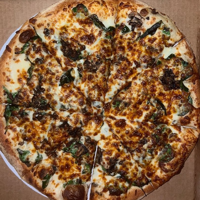 Raven Pizza's whole pizza, topped with melted cheese, mushrooms, and spinach, in a delivery box.