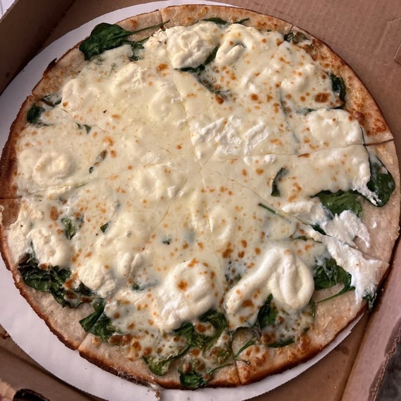 Raven Pizza's white pizza with spinach and ricotta cheese, sliced in a delivery box.