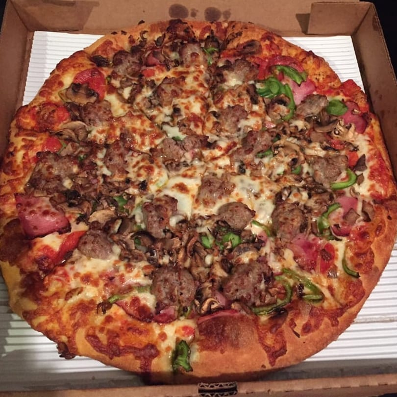 Raven Pizza's whole pizza with sausage, mushrooms, green peppers, and ham in a cardboard box.