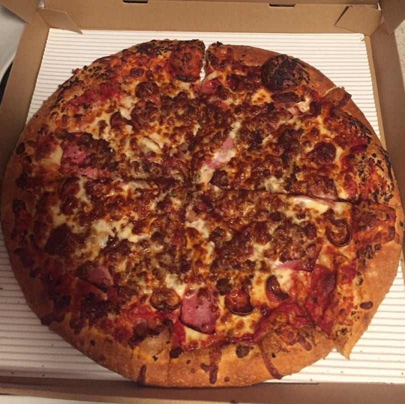 Raven Pizza's meat lover's pizza, with pepperoni, sausage, and ham, in a cardboard box.