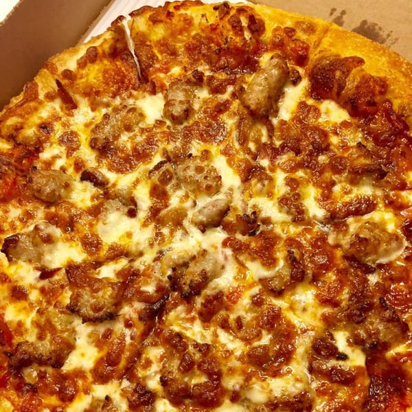 Raven Pizza's sausage pizza, topped with melted cheese and golden-brown crust, in a cardboard box.
